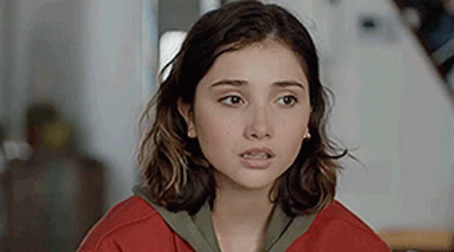 a close up of a young woman wearing a red sweater and earrings .