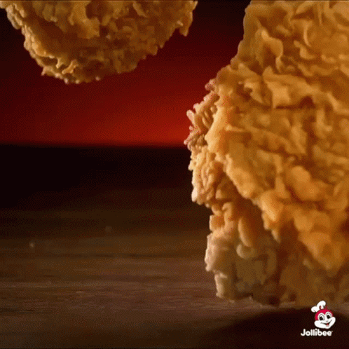 A Close Up Of Fried Chicken On A Wooden Table With A Jollibee Logo In The Corner . GIF
