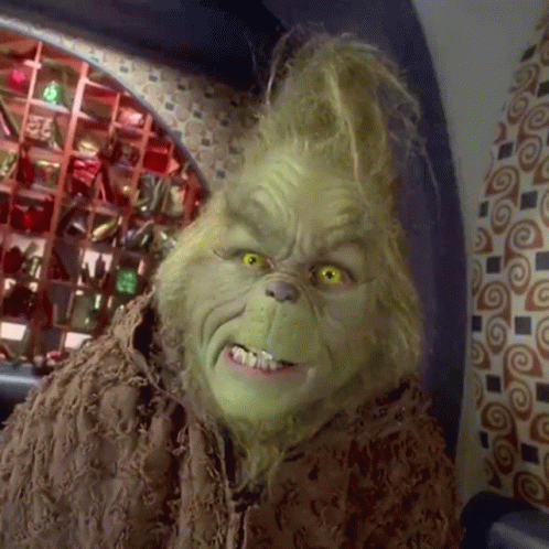 A Close Up Of Grinch 'S Face In A Room With A Patterned Wall GIF