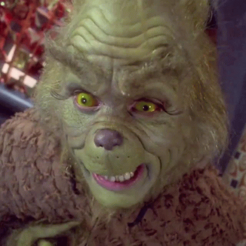 A Close Up Of Grinch 'S Face With Yellow Eyes And A Pink Teeth GIF