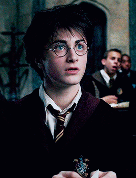 A Close Up Of Harry Potter Wearing Glasses And A Slytherin Crest GIF