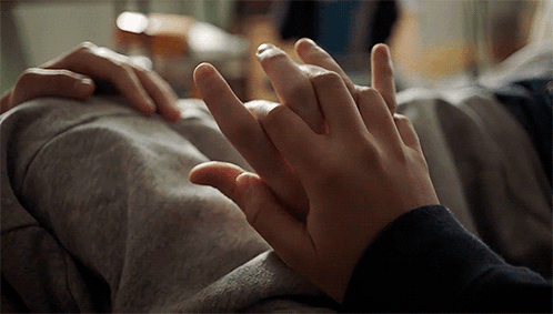 A Close Up Of Two People Holding Hands On A Bed GIF