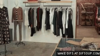 A Clothing Store With Clothes Hanging On Racks And A Table GIF