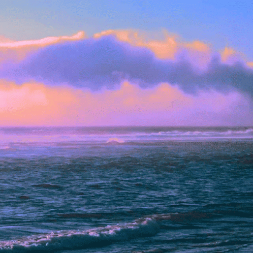 A Cloudy Sky Over The Ocean With Waves Crashing On The Shore GIF
