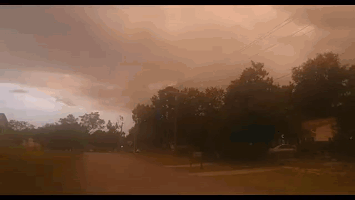 A Cloudy Sky With A Few Trees In The Foreground And A Few Houses In The Background GIF