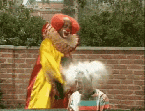 A Clown In A Yellow And Red Costume Is Standing Next To A Woman . GIF