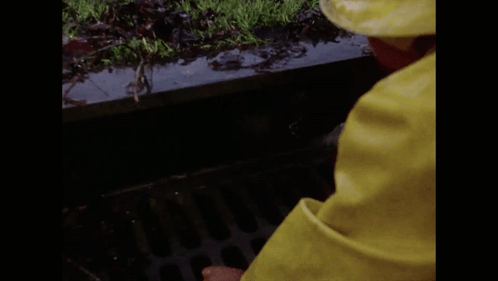 A Clown In A Yellow Raincoat Is Peeking Out Of A Drain And Says Halo GIF
