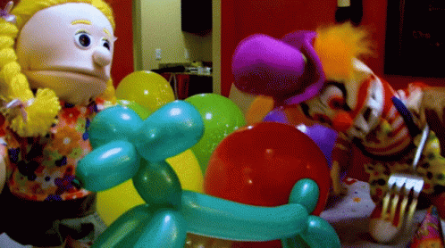A Clown Is Holding A Fork Next To Balloons GIF