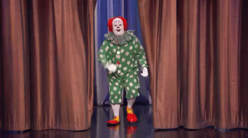 A Clown Is Standing On A Stage In Front Of A Curtain . GIF