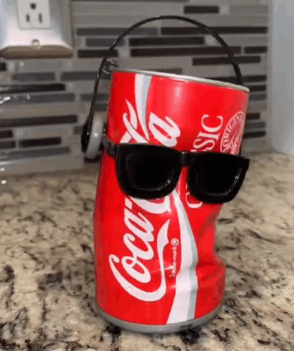 A Coca Cola Can With Sunglasses And Headphones On It Is Sitting On A Counter . GIF
