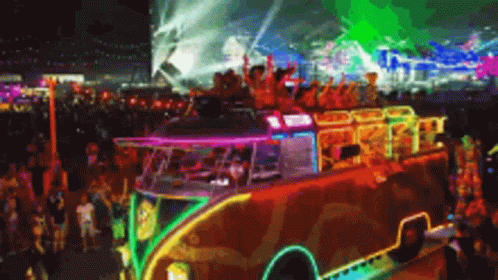 A Colorful Bus Is Driving Through A Crowd Of People At A Festival GIF
