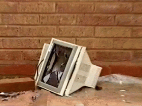A Computer Monitor With A Broken Screen Is Sitting On The Ground In Front Of A Brick Wall GIF