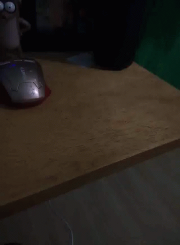 A Computer Mouse Sits On A Wooden Desk Next To A Cartoon Character GIF