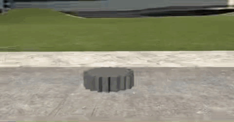 A Concrete Block Is Sitting On The Sidewalk Next To A Grassy Hill . GIF
