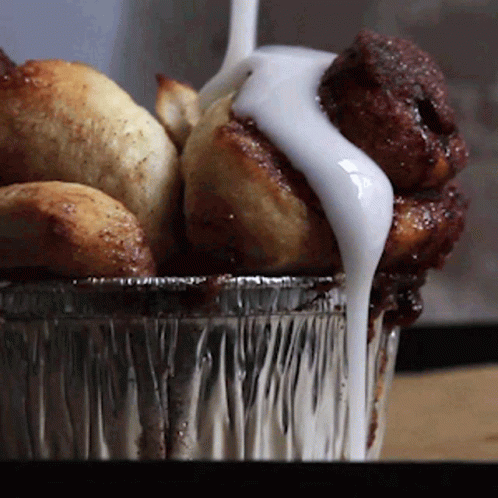 A Container Of Cinnamon Rolls With Icing On Top GIF