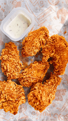 A Container Of Dipping Sauce Sits Next To A Pile Of Fried Chicken Wings GIF