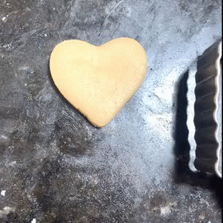 A Cookie In The Shape Of A Heart Is On A Table Next To A Cookie Cutter GIF