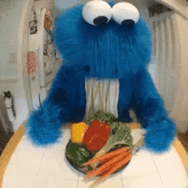 A Cookie Monster Is Sitting At A Table With A Plate Of Vegetables In Front Of Him GIF