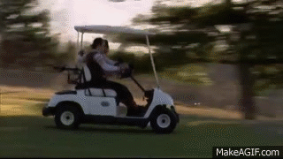 A Couple Is Riding A Golf Cart On A Golf Course . GIF