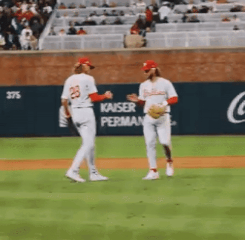 A Couple Of Baseball Players Are Standing On A Baseball Field Talking To Each Other . GIF