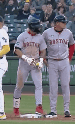A Couple Of Baseball Players Are Standing On A Field . One Of The Players Is Wearing A Boston Jersey . GIF