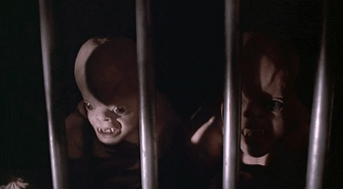 A Couple Of Creepy Dolls Are Behind Bars In A Dark Room GIF