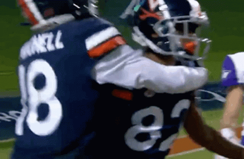 a couple of football players hugging each other on the field .
