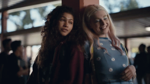 A Couple Of Girls Standing Next To Each Other And One Of Them Is Wearing A Blue Shirt With Daisies On It GIF