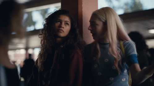 A Couple Of Girls Standing Next To Each Other With One Wearing A Blue Shirt With Daisies On It GIF