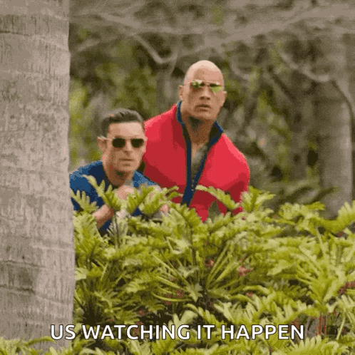 A Couple Of Men Are Standing In The Woods And One Of Them Is Wearing Sunglasses And The Other Is Wearing A Red Jacket . GIF