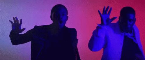 A Couple Of Men Are Standing Next To Each Other In A Dark Room With Their Hands Up In The Air . GIF