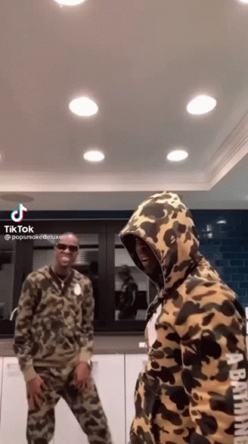 A Couple Of Men Are Standing Next To Each Other In A Kitchen Wearing Camouflage Hoodies . GIF