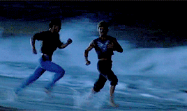 A Couple Of Men Running On A Beach At Night GIF