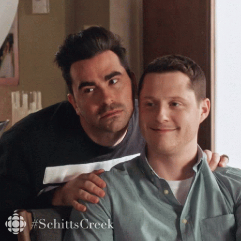 A Couple Of Men Sitting Next To Each Other With The Word Schitts Creek On The Bottom GIF