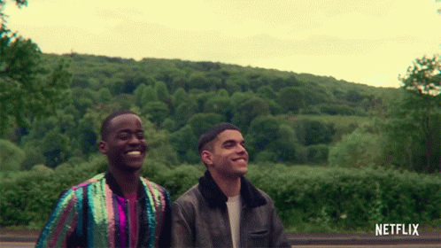 A Couple Of Men Standing Next To Each Other With A Netflix Logo Behind Them GIF