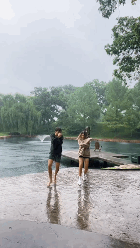A Couple Of People Are Dancing In The Rain Near A Lake . GIF