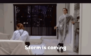 A Couple Of People Are Standing In A Living Room With The Words `` Storm Is Coming '' Written On The Bottom . GIF