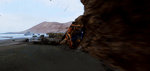 A Couple Of People Are Standing On A Rocky Beach GIF