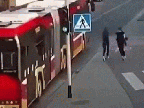 A Couple Of People Are Walking Down A Street Next To A Bus . GIF