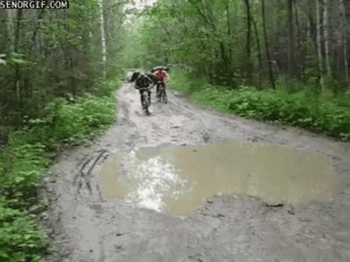A Couple Of People Riding Bikes Down A Muddy Road . GIF