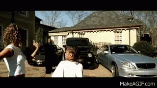 A Couple Of People Standing In Front Of A Silver Car And A House GIF
