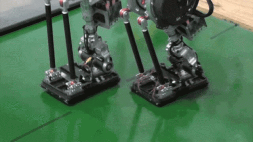 A Couple Of Robots Standing On A Green Surface GIF