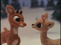 A Couple Of Stuffed Reindeer Standing Next To Each Other In The Snow GIF