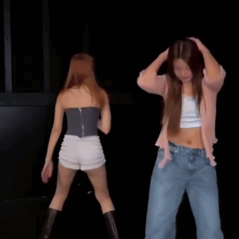 A Couple Of Women Are Dancing Together On A Stage In A Dark Room . GIF