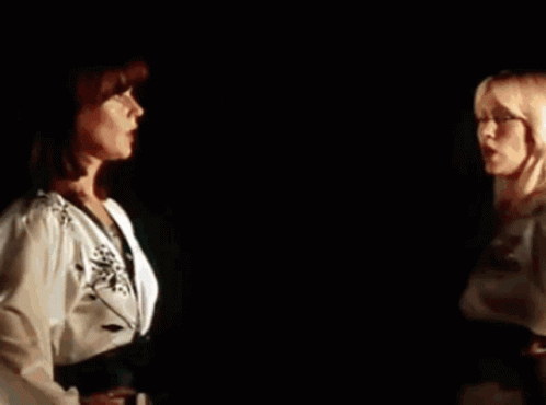 A Couple Of Women Are Standing Next To Each Other In A Dark Room . GIF