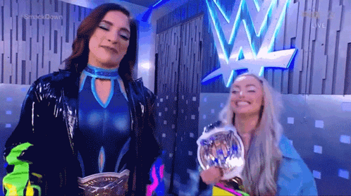 A Couple Of Women Are Standing Next To Each Other In Front Of A Wrestling Logo . GIF