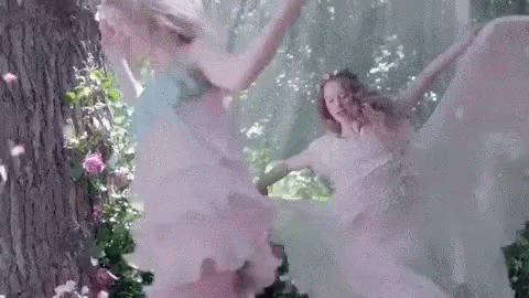 A Couple Of Women In White Dresses Are Dancing In The Woods . GIF