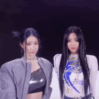A Couple Of Women Standing Next To Each Other On A Stage . GIF