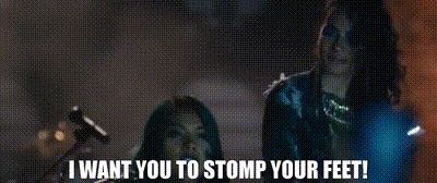 A Couple Of Women Standing Next To Each Other With The Words `` I Want You To Stomp Your Feet '' Written On The Screen . GIF