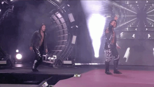 A Couple Of Wrestlers Are Walking On A Stage With A W Logo In The Corner GIF